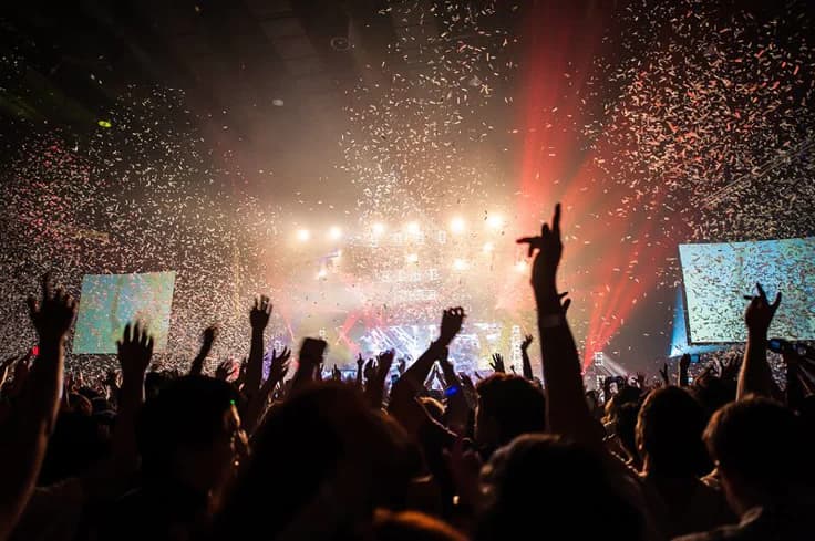 Público celebrando durante un espectáculo en vivo rodeado de luces y confeti.